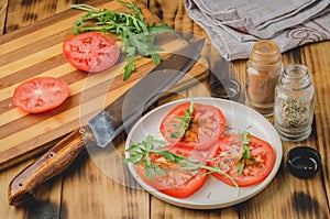 Salad. It is fresh the sliced tomatoes with arugula and seasonings in a white bowl. On a wooden background. Selective focus