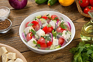 Salad with fresh tomatoes, cucumbers, red onions and feta cheese in a white salad bowl on a rustic wooden table.