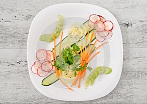Salad with fresh vegetables isolated for appetizer in the white plate on white wooden background.