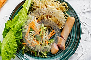 Salad of fresh vegetables on a plate with leaves, next to toasted pasta spaghetti with egg and meat sausage
