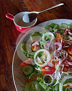 Salad with fresh vegetables on a white plate on a dark brown wooden tablein a roadside cafe.