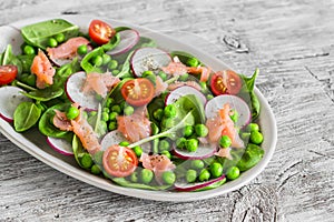 Salad with green peas, radish, cherry tomatoes and spinach on an oval ceramic plate on light wooden table rustic.