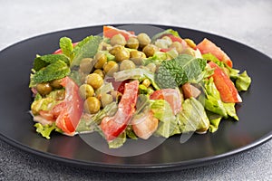 Salad of green tomato leaves and canned peas seasoned with sauce on a black plate. Spring fresh diet salad