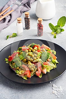 Salad of green tomato leaves and canned peas seasoned with sauce on a black plate. Spring fresh diet salad