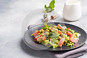 Salad of green tomato leaves and canned peas seasoned with sauce on a black plate. Spring fresh diet salad. copy space