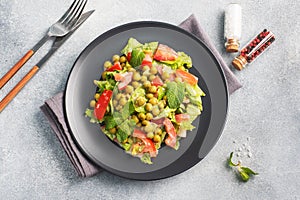 Salad of green tomato leaves and canned peas seasoned with sauce on a black plate. Spring fresh diet salad. top view