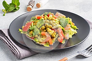 Salad of green tomato leaves and canned peas seasoned with sauce on a black plate. Spring fresh diet salad. top view