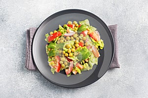 Salad of green tomato leaves and canned peas seasoned with sauce on a black plate. Spring fresh diet salad. top view copy space