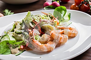 Salad from greens and shrimps on a white ceramic plate