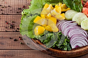 Salad of greens, tomatoes, cucumbers, sweet pepper onions on a wooden background