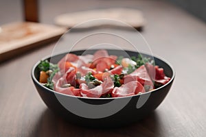 Salad with kale, bresaola and cherry tomatoes decorated with capers in black bowl on walnut wood table