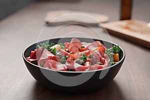 Salad with kale, bresaola and cherry tomatoes decorated with capers in black bowl on walnut wood table