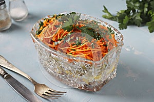 Salad with Korean carrots, ham, eggs, onion and mushrooms in a transparent salad bowl on a light blue background