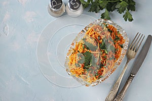 Salad with Korean carrots, ham, eggs, onion and mushrooms in a transparent salad bowl on a light blue background, Top