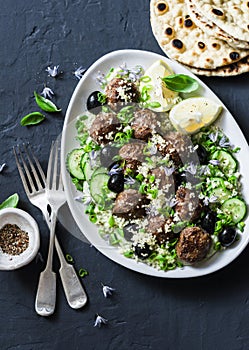 Salad with lamb meatballs, avocado, greek yogurt sauce, couscous and whole grain flatbread on a dark background, top view.