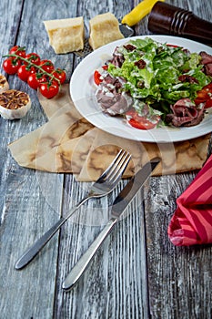 Salad leaves with sliced roast beef and sun-dried cherry tomatoes on wooden background