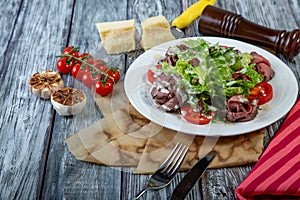 Salad leaves with sliced roast beef and sun-dried cherry tomatoes on wooden background