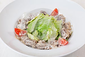 Salad with meat in a creamy sauce, ase, lettuce, romaine, iceberg cherry tomatoes on top of the plate