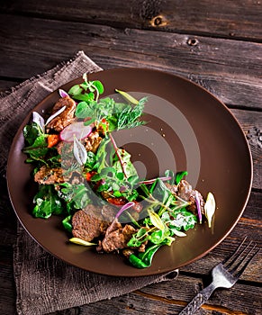 Salad with meat,greens and garden radish on brown plate.
