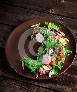 Salad with meat,greens and garden radish on brown plate.