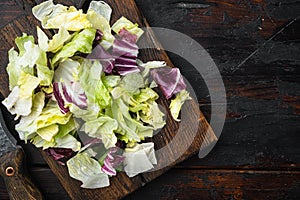 Salad with a mix of different salad leaves, like romaine lettuce, endive or arugula, on wooden cutting board, on old dark  wooden