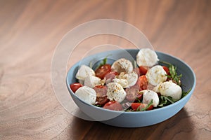 Salad with mozxarella, tomatoes and arugula in a blue bowl on walnut wood table