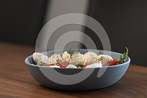 Salad with mozxarella, tomatoes and arugula in a blue bowl on walnut wood table