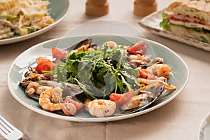 Salad of mussels, clams, arugula and tomato served on a plate in a restaurant. Keto diet and healthy food