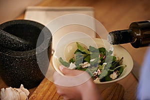 Salad, olive oil and hand with bowl for healthy food, eating meal of leaves or lettuce with cheese in kitchen. Person