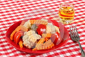 Salad of pickled vegetables cauliflower, paprika and carrot slices in a red plate and a glass of rakia grape, brandy like