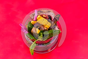 Salad with pieces of beef meat, grilled vegetables - eggplant, corn, mushrooms, sauce in a glass jar on a red background