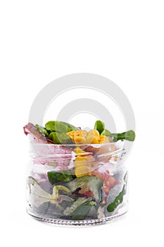 Salad with pieces of beef meat, grilled vegetables - eggplant, corn, mushrooms, sauce in a glass jar on a white background.