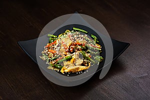 Salad with pieces of chicken, green beans and vegetables in a black plate on a brown wooden background