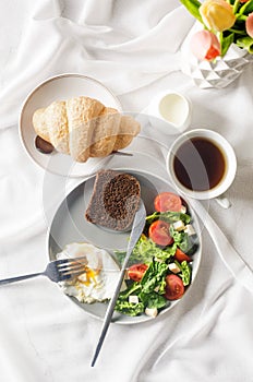 Salad in plate, egg, cup of coffee and croissant , fresh tulips in vase on clean white