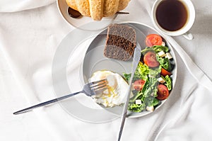 Salad in plate, egg, cup of coffee and croissant , fresh tulips in vase on clean white