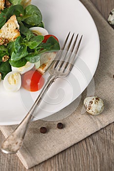 Salad with quail egg, cherry tomato, crackers and corn salad on wooden background