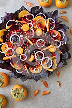 Salad with red basil leaves, persimmon, pomegranate and pumpkin seeds,beetroot, and onion on grey background. Flat lay