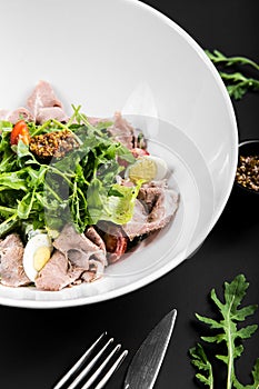 Salad with roast beef, arugula, cherry tomatoes, egg and grain mustard on a black background. close up