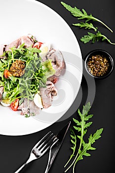 Salad with roast beef, arugula, cherry tomatoes, egg and grain mustard on a black background. top view. close up