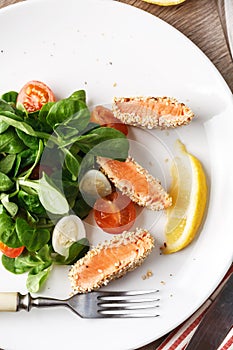 Salad with salmon grilled in sesame seeds, cherry tomatoes and quail egg on wooden table