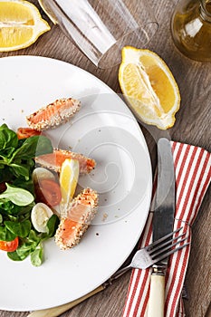 Salad with salmon grilled in sesame seeds, cherry tomatoes and quail egg on wooden table