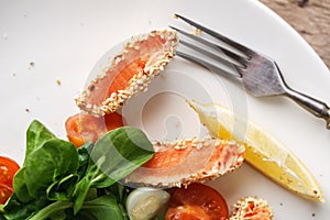 Salad with salmon grilled in sesame seeds, cherry tomatoes and quail egg on wooden table