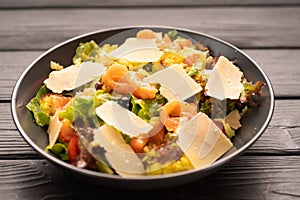 Salad with salted salmon, lettuce, slices of Parmesan cheese on top, served on a plate on a wooden table. Mediterranean