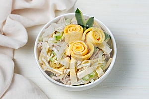 Salad of shredded boiled chicken, fresh cucumber, onion and chopped egg pancakes closeup in bowl on table. Decorated