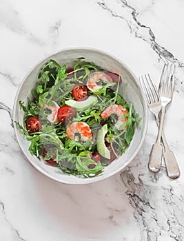 Salad with shrimp, arugula,avocado, cherry tomatoes on a light marble background, top view