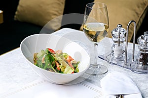 Salad with shrimp, cucumber, olives, tomatoes and basil. Glass of white wine. Place for text