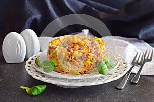 Salad with smoked sausage, corn, cheese, fresh carrot, egg, garlic and yogurt on a white plate on a abstract background.