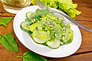 Salad from spinach and cucumber with fork on wooden board