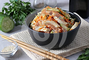 Salad with squid, carrots and cucumber, sprinkled with sesame seeds, in a dark bowl on a light background
