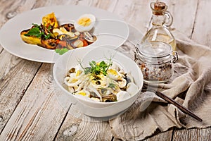 Salad with squid rings, mozzarella cheese, olives, capers and microgreens and baked vegetables with mushrooms in a white bowl.